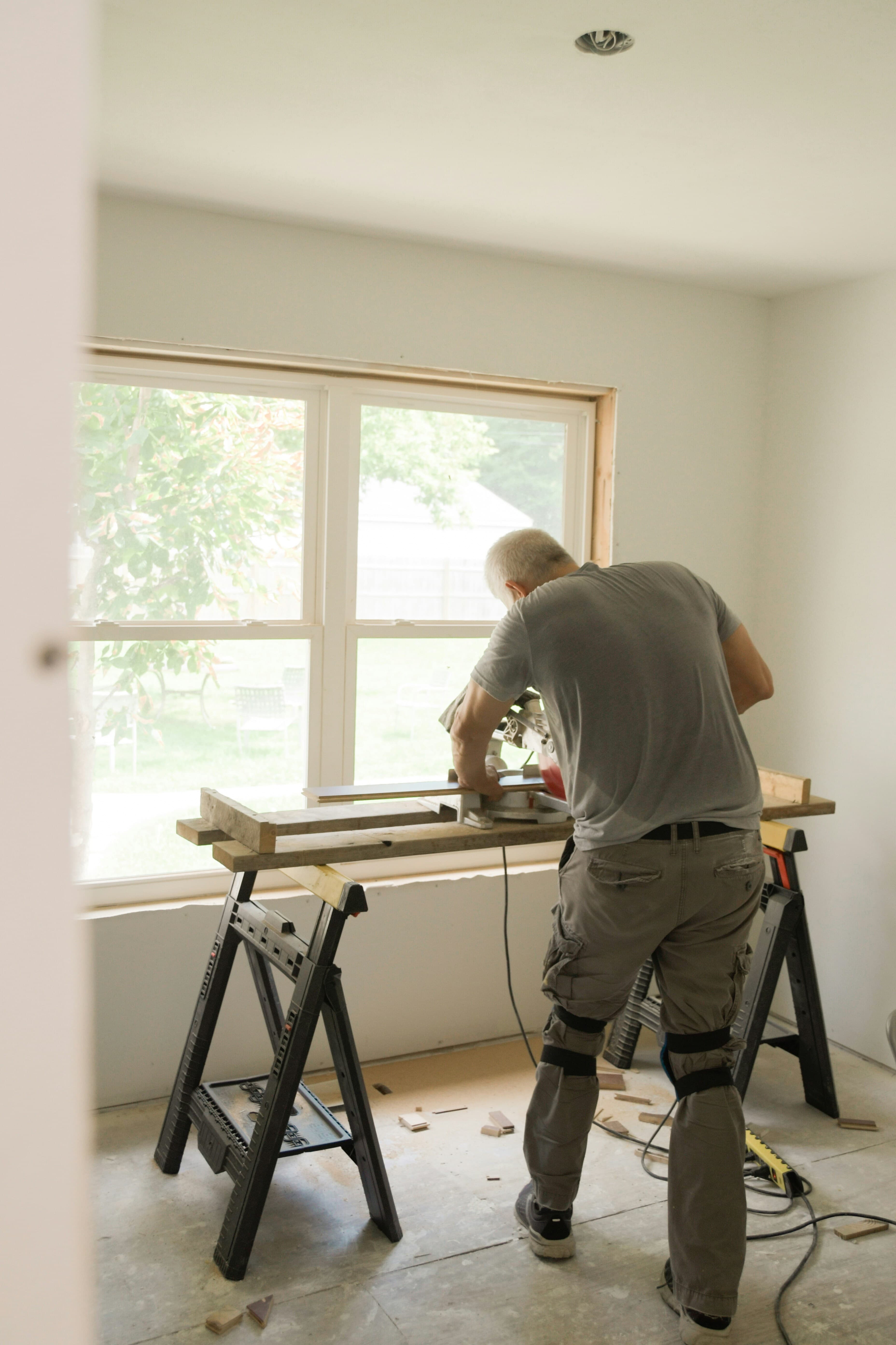 Man using a miter saw to cut wood inside a room undergoing home renovation.